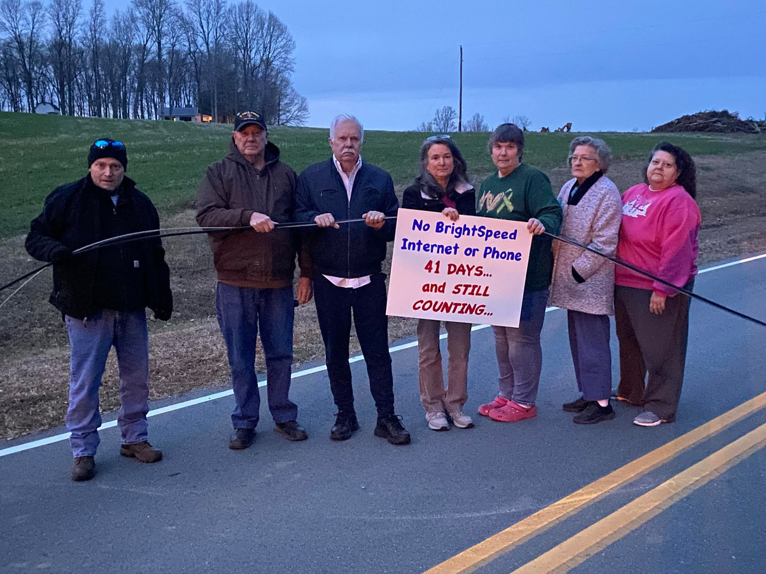 Joanna Hedrick (center) and some of her Charlie Cooper Road neighbors in Siler City pose holding a downed Brightspeed cable that lay across that road for part of November and most of the month of December..